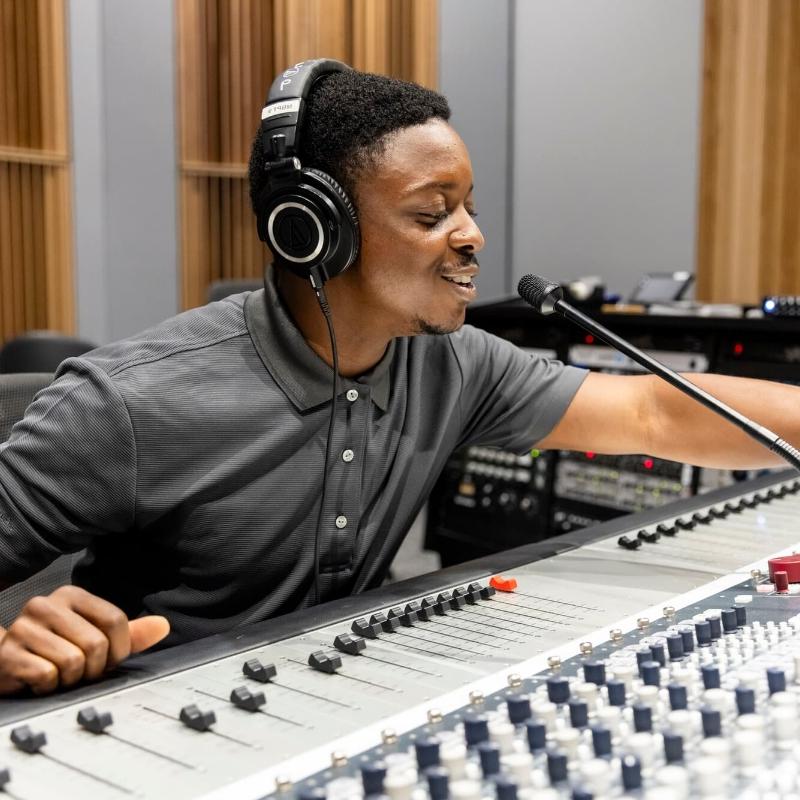 ACC student talking into a microphone with headphones on infront of an audio panel.